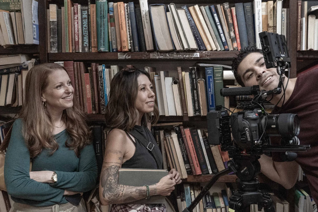 Cast and crew gathered around a cinema camera in a bookshop on the set of Recovery.