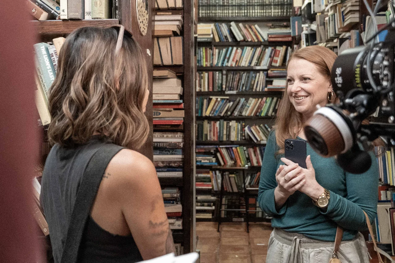Two Recovery cast members sharing a smile beside the camera in a bookshop.